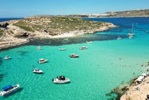 Boats floating in the Blue Lagoon Malta, surrounded by perfectly clear blue waters near Comino Island.