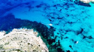Blue water around Comino with a private boat floating in the crystal-clear turquoise sea near the Blue Lagoon, Malta.