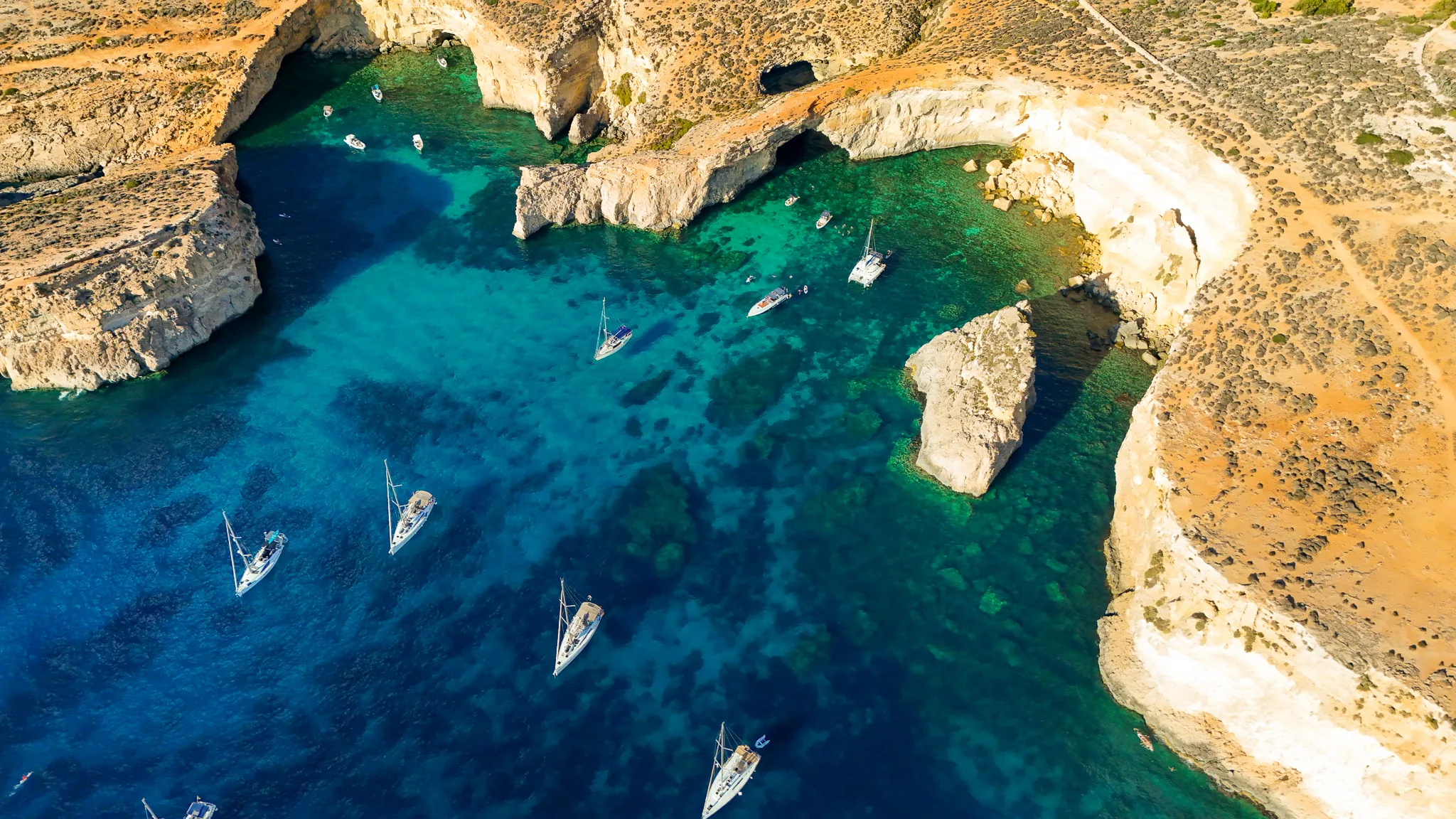 Drone view of Crystal Lagoon at Comino Malta, showing deep blue water, cliffs, and boats anchored in clear sea.