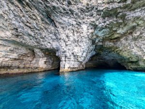 Santa Marija Caves in Comino Malta with a boat entering the bright turquoise sea caves and crystal-clear blue water.