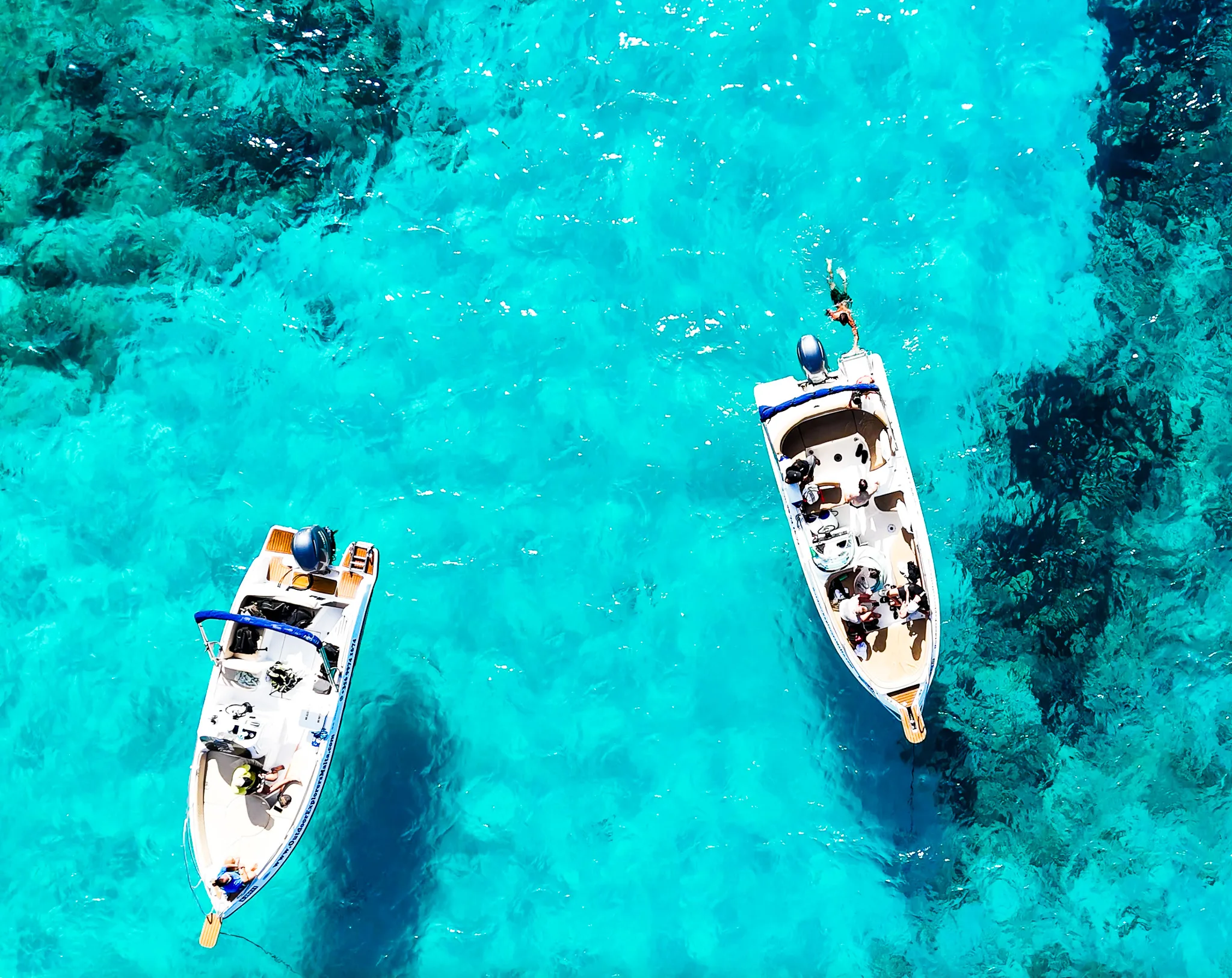 Two boats floating in clear blue waters near Comino Malta, highlighting calm sea conditions and a relaxed private boat atmosphere.